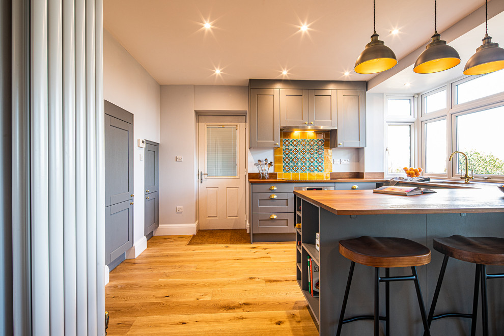 This is an example of a mid-sized eclectic u-shaped eat-in kitchen in Other with an undermount sink, shaker cabinets, grey cabinets, wood benchtops, yellow splashback, terra-cotta splashback, a peninsula, brown floor and brown benchtop.