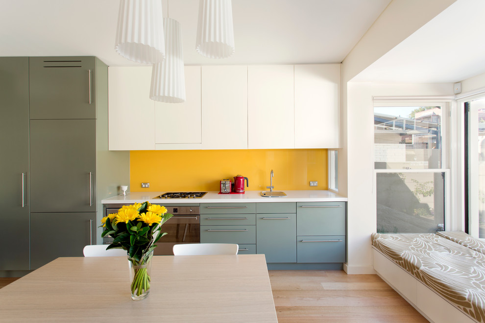 Inspiration for a small contemporary single-wall eat-in kitchen in Sydney with flat-panel cabinets, stainless steel appliances, yellow splashback, green cabinets, a single-bowl sink, glass sheet splashback, light hardwood floors and no island.