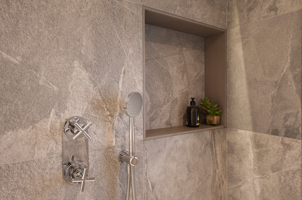 This is an example of a large contemporary master bathroom in Barcelona with furniture-like cabinets, white cabinets, a corner shower, a wall-mount toilet, gray tile, ceramic tile, grey walls, ceramic floors, a wall-mount sink, grey floor, a sliding shower screen and white benchtops.