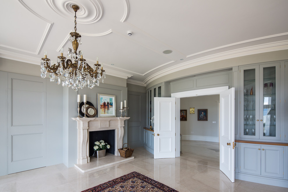 This is an example of a large traditional separate dining room in London with grey walls, porcelain floors, a standard fireplace, a stone fireplace surround and beige floor.