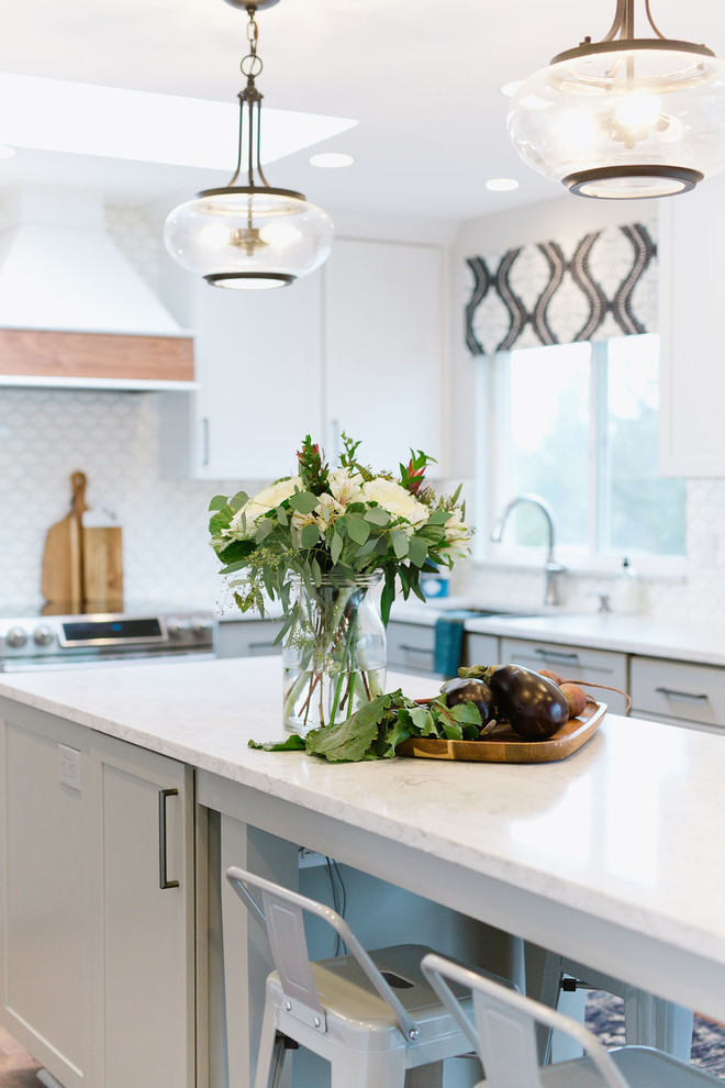 Mid-sized transitional u-shaped medium tone wood floor and brown floor open concept kitchen photo with an undermount sink, shaker cabinets, white cabinets, quartz countertops, white backsplash, porcelain backsplash, stainless steel appliances, an island and white countertops