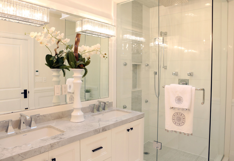 This is an example of a mid-sized transitional master bathroom in Toronto with flat-panel cabinets, white cabinets, a freestanding tub, a corner shower, a one-piece toilet, gray tile, ceramic tile, white walls, mosaic tile floors, a drop-in sink and marble benchtops.