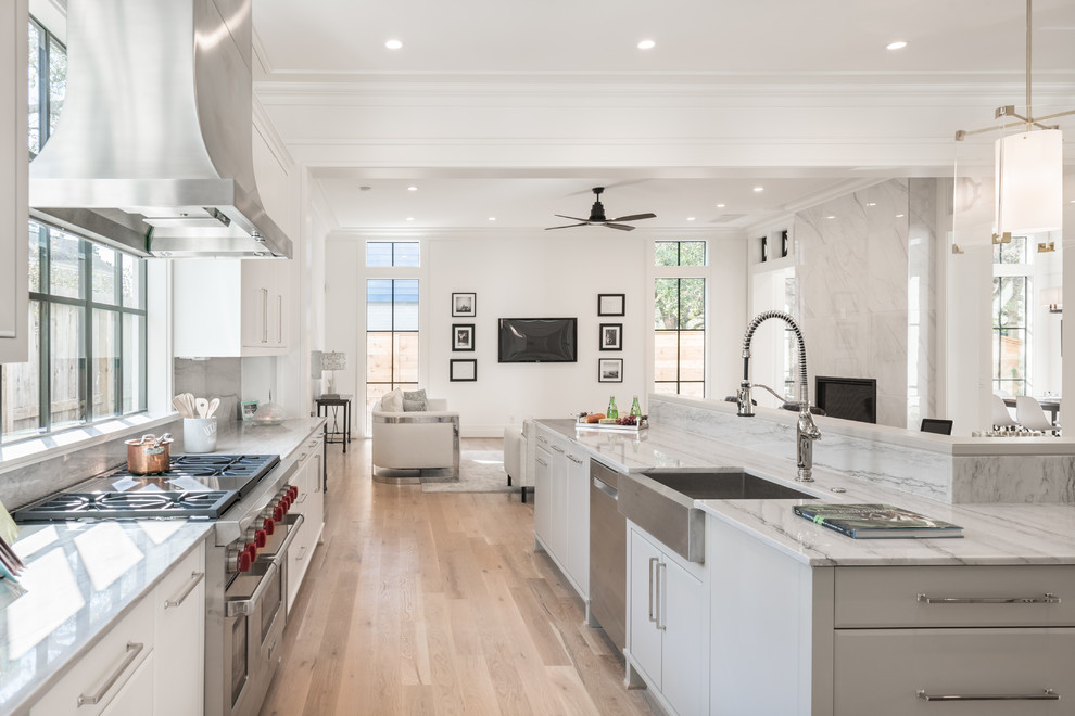 Inspiration for a large contemporary l-shaped open plan kitchen in Houston with a farmhouse sink, flat-panel cabinets, white cabinets, quartzite benchtops, white splashback, stone slab splashback, stainless steel appliances, light hardwood floors, with island, beige floor and white benchtop.
