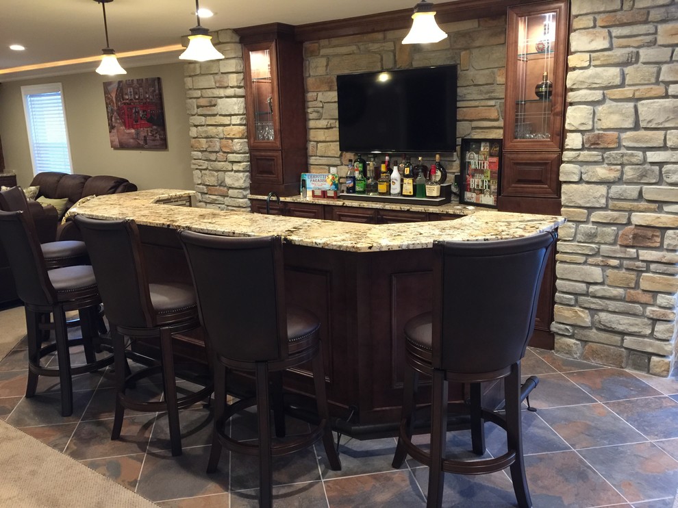 This is an example of a large arts and crafts single-wall seated home bar in St Louis with ceramic floors, an undermount sink, raised-panel cabinets, granite benchtops, beige splashback, stone tile splashback, multi-coloured floor and medium wood cabinets.