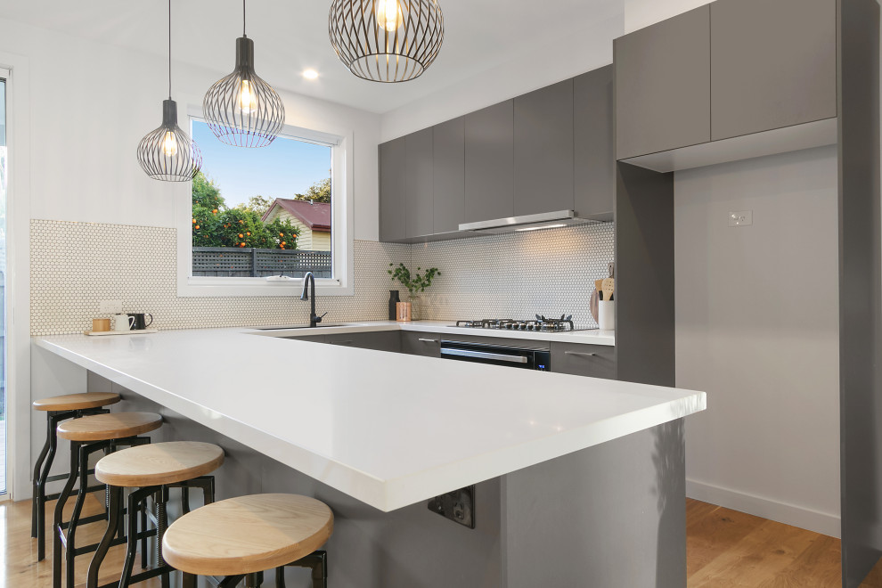 Design ideas for a mid-sized traditional u-shaped open plan kitchen in Melbourne with an undermount sink, grey cabinets, granite benchtops, white splashback, ceramic splashback, black appliances, medium hardwood floors, with island, brown floor and white benchtop.