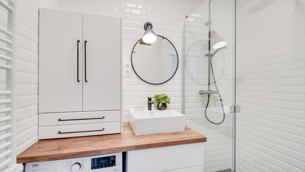 This is an example of a small contemporary master bathroom in Paris with flat-panel cabinets, white cabinets, a curbless shower, a two-piece toilet, white tile, subway tile, white walls, ceramic floors, a console sink, wood benchtops, black floor, a sliding shower screen, brown benchtops, a laundry, a single vanity and a freestanding vanity.