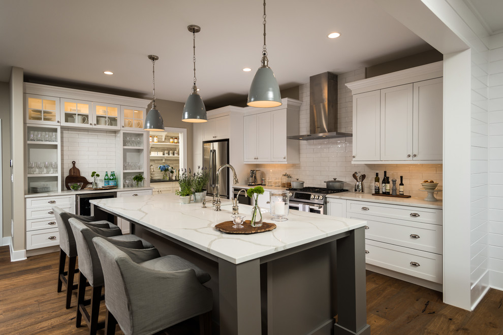 Transitional l-shaped dark wood floor and brown floor kitchen photo in Boston with a farmhouse sink, shaker cabinets, white cabinets, white backsplash, subway tile backsplash, stainless steel appliances and an island