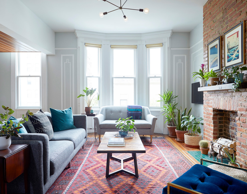 Photo of a mid-sized eclectic formal enclosed living room in New York with grey walls, a standard fireplace, a brick fireplace surround, medium hardwood floors, no tv and brown floor.