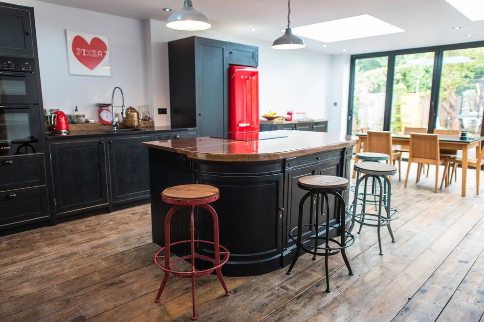 Large country galley open plan kitchen in London with a drop-in sink, shaker cabinets, distressed cabinets, copper benchtops, panelled appliances, dark hardwood floors and with island.