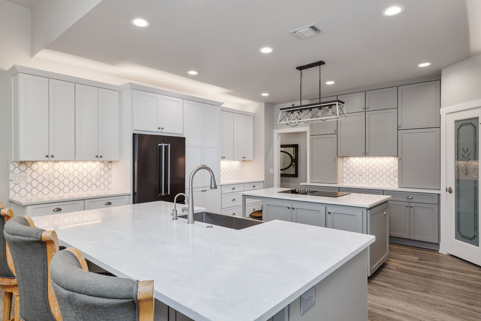 Inspiration for a mid-sized transitional u-shaped vinyl floor and brown floor kitchen pantry remodel in Austin with a farmhouse sink, shaker cabinets, white cabinets, quartz countertops, white backsplash, marble backsplash, black appliances, two islands and white countertops