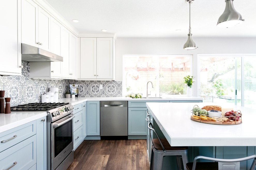 Photo of a mid-sized transitional l-shaped kitchen pantry in Los Angeles with an undermount sink, shaker cabinets, blue cabinets, quartz benchtops, multi-coloured splashback, porcelain splashback, stainless steel appliances, vinyl floors, with island, brown floor and white benchtop.