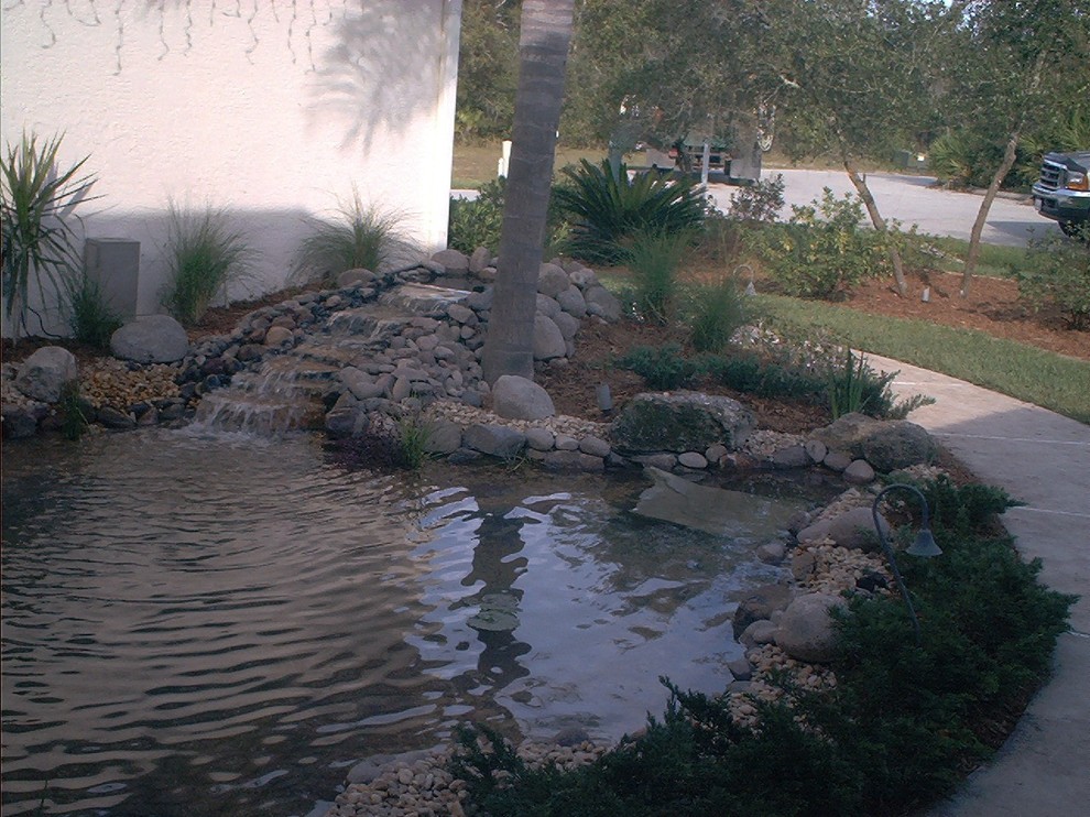 Inspiration for a mid-sized transitional front yard partial sun garden in Miami with with pond and natural stone pavers.