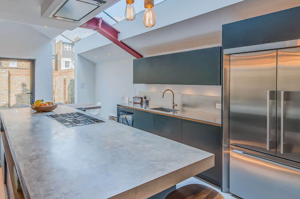Photo of a mid-sized industrial galley open plan kitchen in Surrey with a single-bowl sink, flat-panel cabinets, black cabinets, concrete benchtops, metallic splashback, stainless steel appliances, concrete floors and with island.