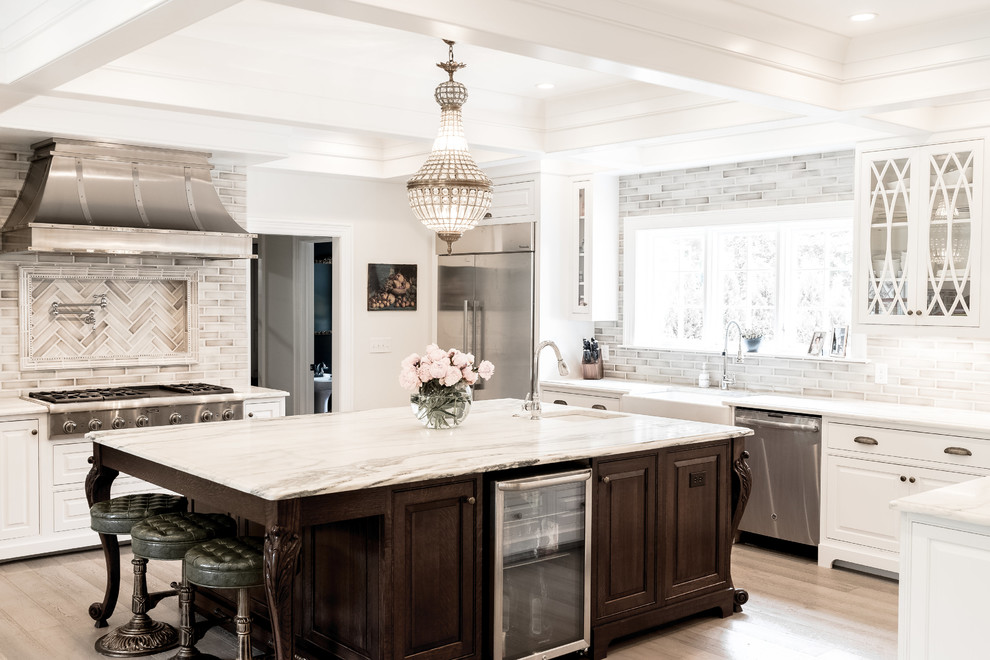 Photo of a large traditional u-shaped eat-in kitchen in Indianapolis with a farmhouse sink, raised-panel cabinets, white cabinets, marble benchtops, ceramic splashback, stainless steel appliances, light hardwood floors, with island and grey floor.