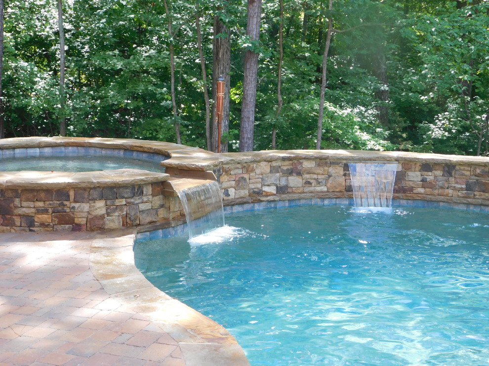 This is an example of a mid-sized country backyard custom-shaped natural pool in Atlanta with a hot tub and brick pavers.