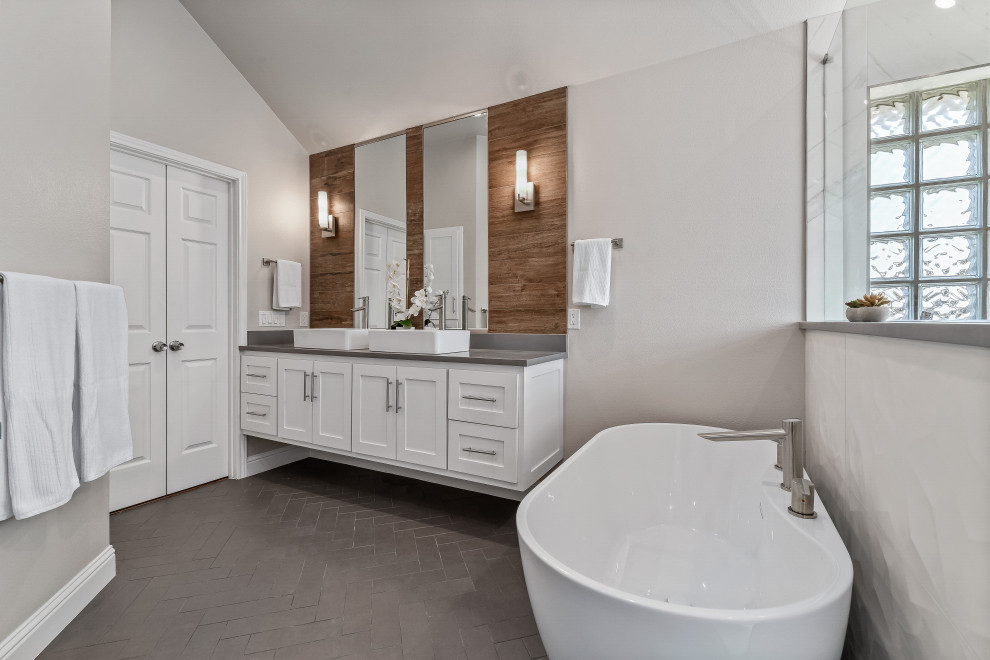 Design ideas for a large contemporary master bathroom in Dallas with shaker cabinets, white cabinets, a freestanding tub, an alcove shower, white tile, porcelain tile, grey walls, porcelain floors, a vessel sink, engineered quartz benchtops, black floor, a hinged shower door, grey benchtops, a niche, a double vanity, a floating vanity and vaulted.
