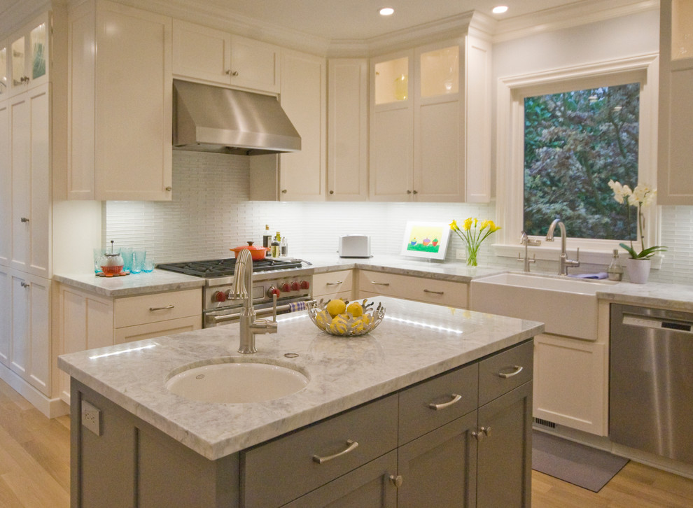Design ideas for a mid-sized transitional kitchen in San Francisco with a farmhouse sink, recessed-panel cabinets, white cabinets, granite benchtops, grey splashback, glass tile splashback, stainless steel appliances, light hardwood floors and with island.