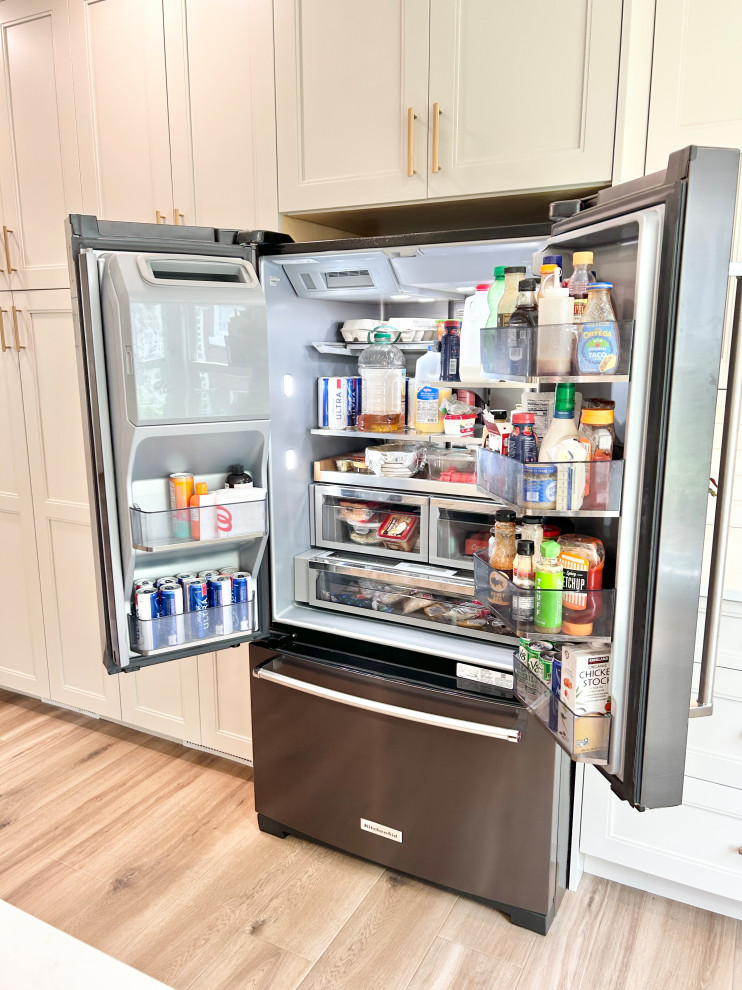 Inspiration for a large transitional u-shaped light wood floor open concept kitchen remodel with an undermount sink, flat-panel cabinets, white cabinets, quartz countertops, white backsplash, ceramic backsplash, black appliances, an island and white countertops