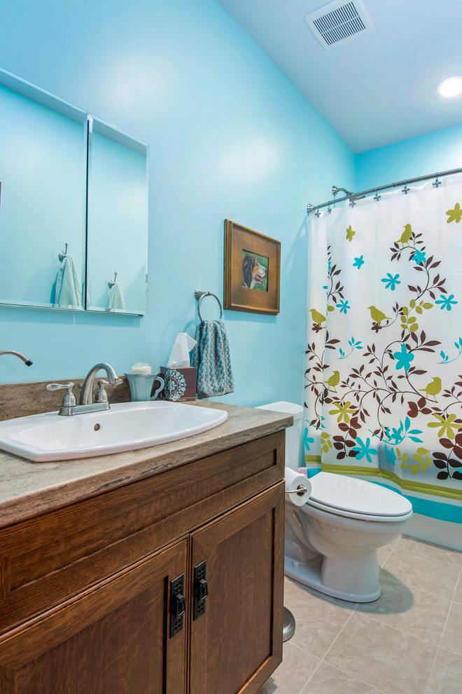 Photo of a large arts and crafts kids bathroom in Columbus with recessed-panel cabinets, dark wood cabinets, an alcove tub, a shower/bathtub combo, a two-piece toilet, blue walls, ceramic floors, a drop-in sink, granite benchtops, beige floor and a shower curtain.