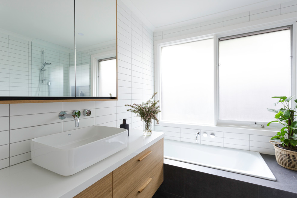 This is an example of a mid-sized contemporary 3/4 bathroom in Melbourne with beaded inset cabinets, light wood cabinets, a corner tub, an open shower, white tile, subway tile, a drop-in sink, solid surface benchtops, an open shower and white benchtops.