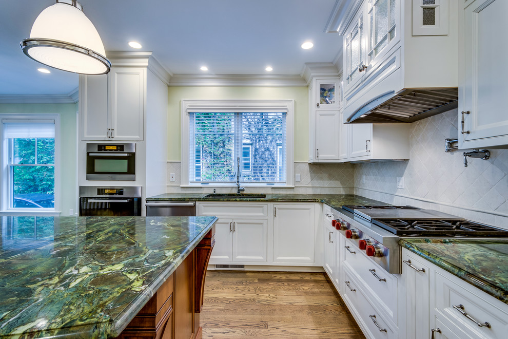 Mid-sized transitional l-shaped open plan kitchen in Boston with a farmhouse sink, recessed-panel cabinets, white cabinets, onyx benchtops, beige splashback, ceramic splashback, stainless steel appliances, medium hardwood floors, with island and brown floor.