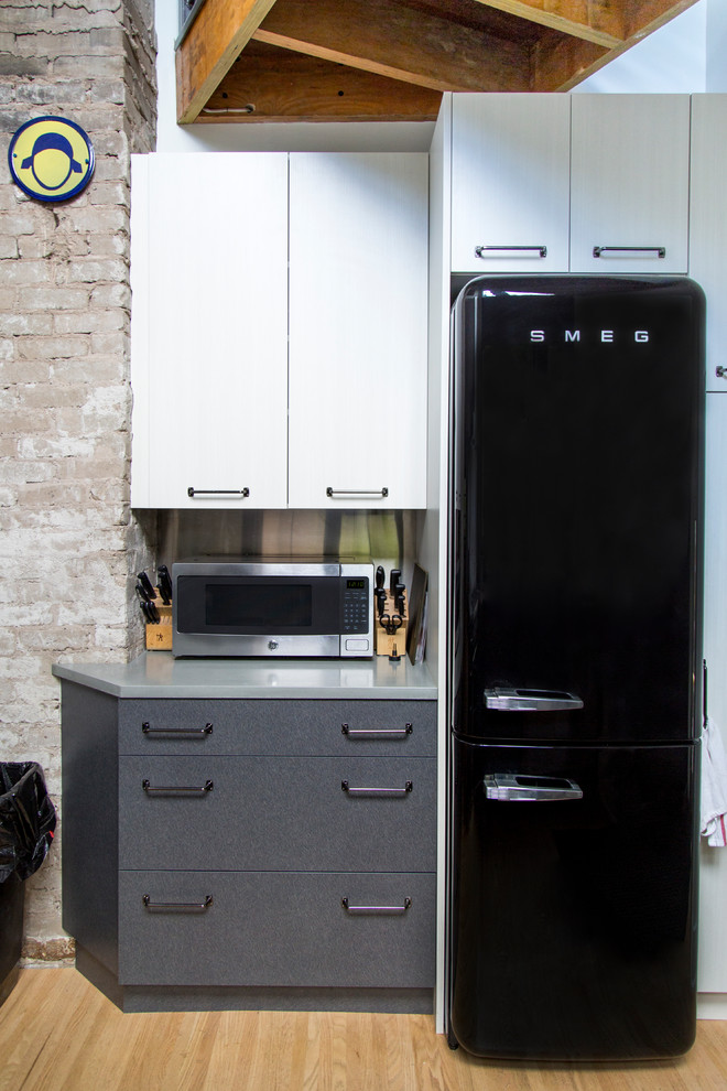 Kitchen - small contemporary l-shaped light wood floor kitchen idea with an undermount sink, flat-panel cabinets, gray cabinets, concrete countertops, metallic backsplash, black appliances, a peninsula and gray countertops