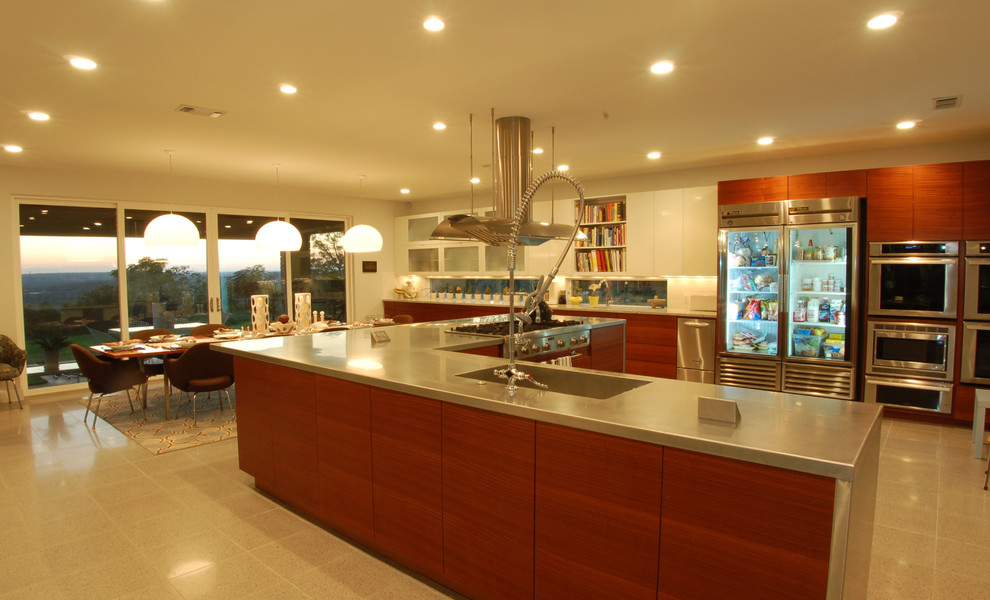 This is an example of a contemporary eat-in kitchen in Austin with flat-panel cabinets, medium wood cabinets and stainless steel benchtops.