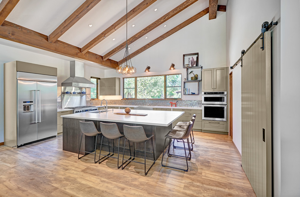 This is an example of a large country u-shaped open plan kitchen in Sacramento with a farmhouse sink, recessed-panel cabinets, green cabinets, quartz benchtops, metallic splashback, mosaic tile splashback, stainless steel appliances, vinyl floors, with island, brown floor and white benchtop.