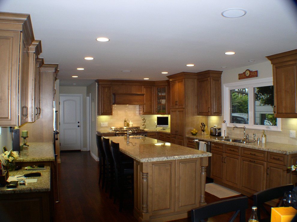 Eat-in kitchen - mid-sized traditional u-shaped medium tone wood floor eat-in kitchen idea in Los Angeles with an undermount sink, raised-panel cabinets, medium tone wood cabinets, granite countertops, beige backsplash, ceramic backsplash, stainless steel appliances and an island