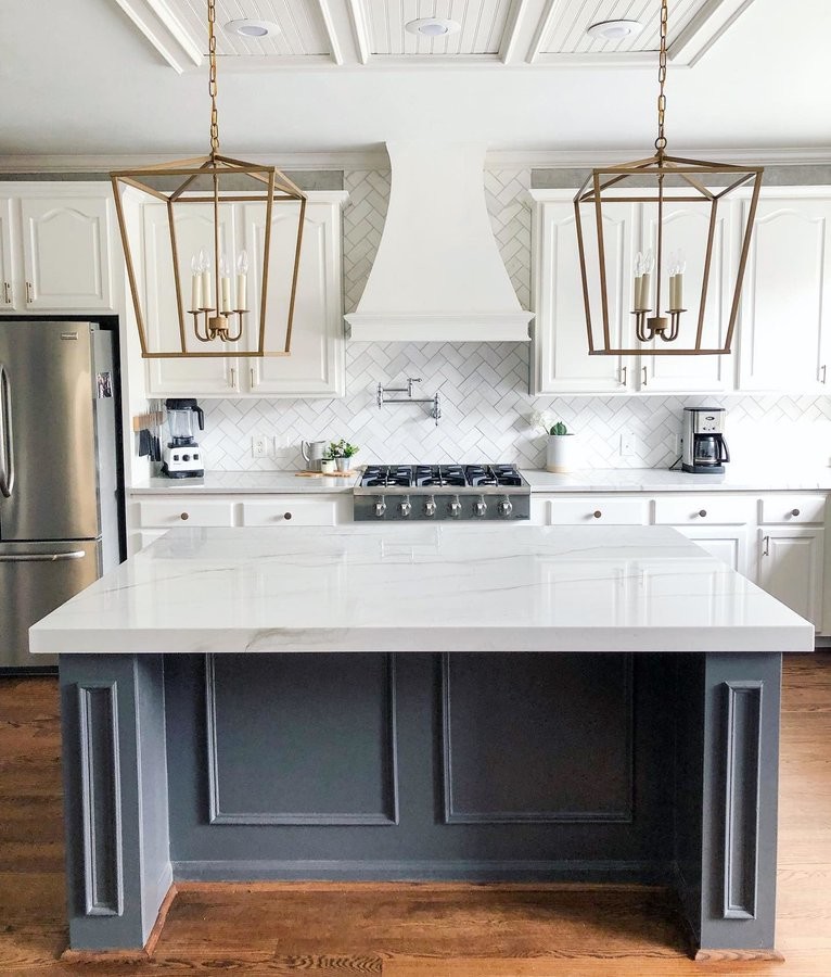This is an example of a large country single-wall kitchen in Raleigh with raised-panel cabinets, white cabinets, marble benchtops, white splashback, subway tile splashback, stainless steel appliances, medium hardwood floors, with island, brown floor and white benchtop.