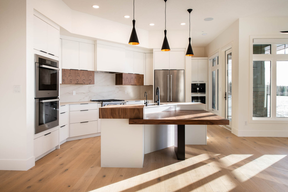 Modern inredning av ett mellanstort vit linjärt vitt kök med öppen planlösning, med en undermonterad diskho, släta luckor, vita skåp, träbänkskiva, vitt stänkskydd, rostfria vitvaror, ljust trägolv, en köksö och brunt golv