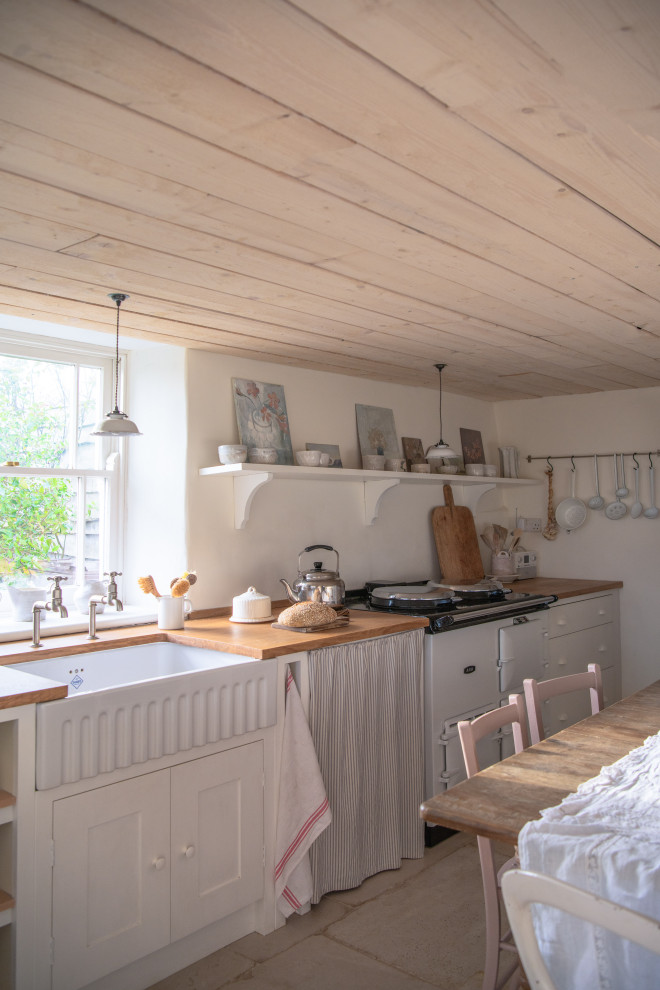 This is an example of a small single-wall eat-in kitchen in London with a farmhouse sink, shaker cabinets, white cabinets, wood benchtops, white appliances, no island, beige floor, brown benchtop and timber.