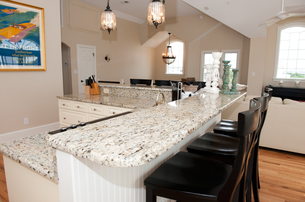 Large transitional light wood floor open concept kitchen photo with an undermount sink, raised-panel cabinets, beige cabinets, granite countertops, multicolored backsplash, mosaic tile backsplash, stainless steel appliances and a peninsula