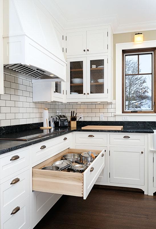 This is an example of a large transitional l-shaped separate kitchen with a farmhouse sink, beaded inset cabinets, white cabinets, white splashback, subway tile splashback, panelled appliances, dark hardwood floors, with island, brown floor and black benchtop.