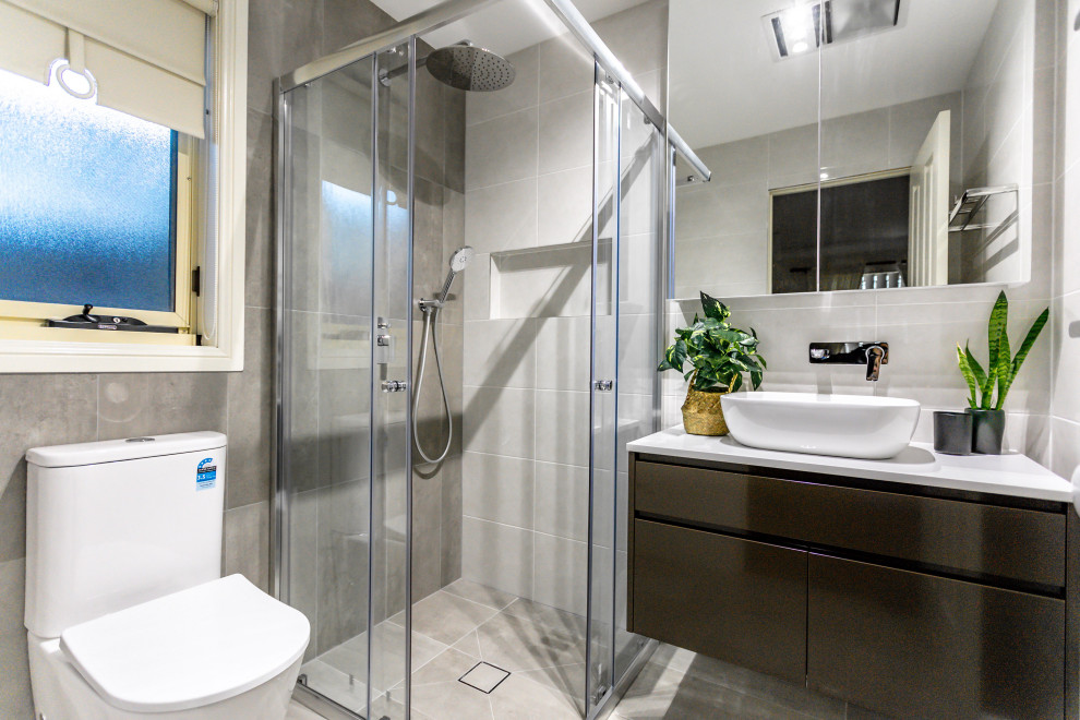 Пример оригинального дизайна: маленькая главная ванная комната в современном стиле с плоскими фасадами, коричневыми фасадами, отдельно стоящей ванной, угловым душем, раздельным унитазом, серой плиткой, керамической плиткой, серыми стенами, полом из керамической плитки, настольной раковиной, столешницей из искусственного кварца, серым полом, душем с раздвижными дверями, белой столешницей, нишей, тумбой под одну раковину и подвесной тумбой для на участке и в саду