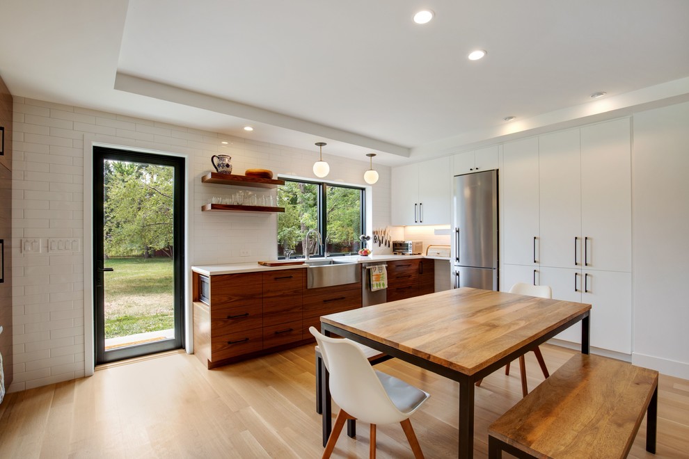 Photo of a mid-sized modern l-shaped eat-in kitchen in Denver with a farmhouse sink, flat-panel cabinets, dark wood cabinets, quartz benchtops, white splashback, ceramic splashback, stainless steel appliances, light hardwood floors, no island, brown floor and white benchtop.