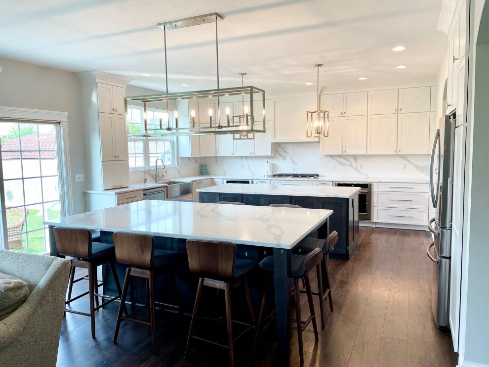 Eat-in kitchen - large transitional u-shaped medium tone wood floor and brown floor eat-in kitchen idea in Chicago with a farmhouse sink, shaker cabinets, white cabinets, quartz countertops, white backsplash, quartz backsplash, stainless steel appliances, two islands and white countertops