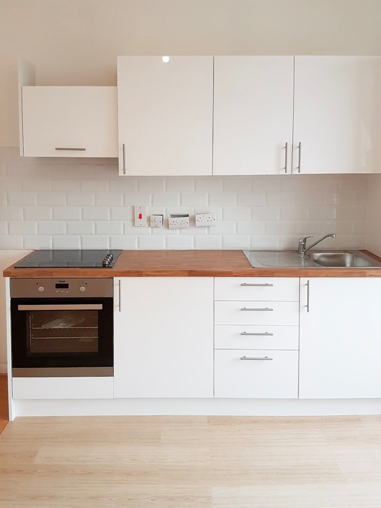 Small scandinavian l-shaped eat-in kitchen in Surrey with glass-front cabinets, white cabinets, wood benchtops, stainless steel appliances, linoleum floors, no island and beige benchtop.