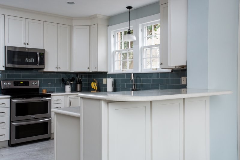 Eat-in kitchen - mid-sized transitional u-shaped vinyl floor eat-in kitchen idea with an undermount sink, shaker cabinets, white cabinets, quartz countertops, blue backsplash, glass tile backsplash, stainless steel appliances and a peninsula