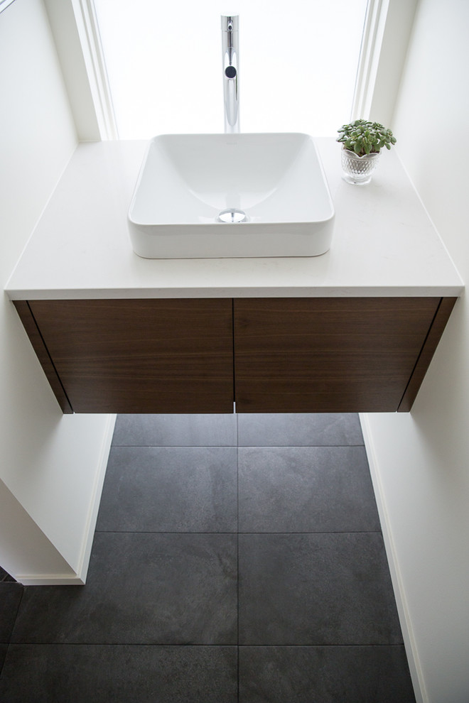 Small modern 3/4 bathroom in Calgary with flat-panel cabinets, medium wood cabinets, a curbless shower, a two-piece toilet, white tile, ceramic tile, white walls, limestone floors, a vessel sink, engineered quartz benchtops, black floor and a hinged shower door.