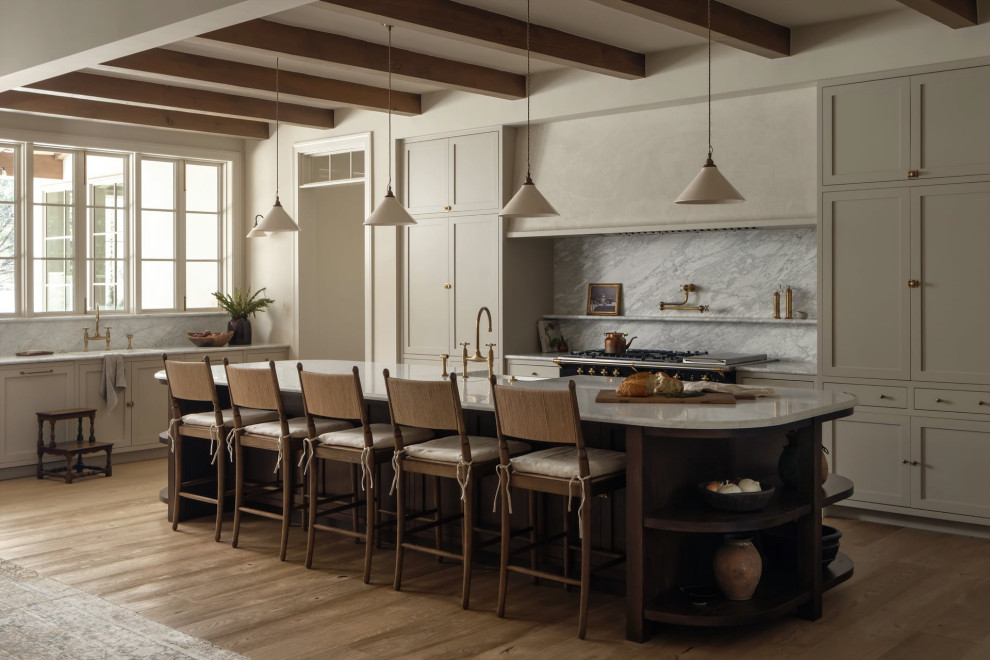 Kitchen - transitional l-shaped medium tone wood floor, brown floor and exposed beam kitchen idea in Austin with shaker cabinets, beige cabinets, an island, gray countertops, a farmhouse sink, gray backsplash, stone slab backsplash and black appliances