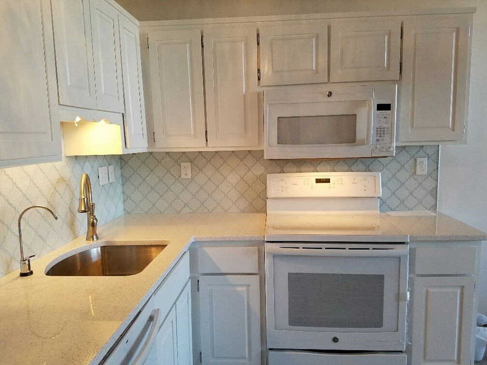 Photo of a mid-sized traditional l-shaped separate kitchen in Bridgeport with an undermount sink, raised-panel cabinets, white cabinets, terrazzo benchtops, white splashback, ceramic splashback, white appliances, light hardwood floors and no island.