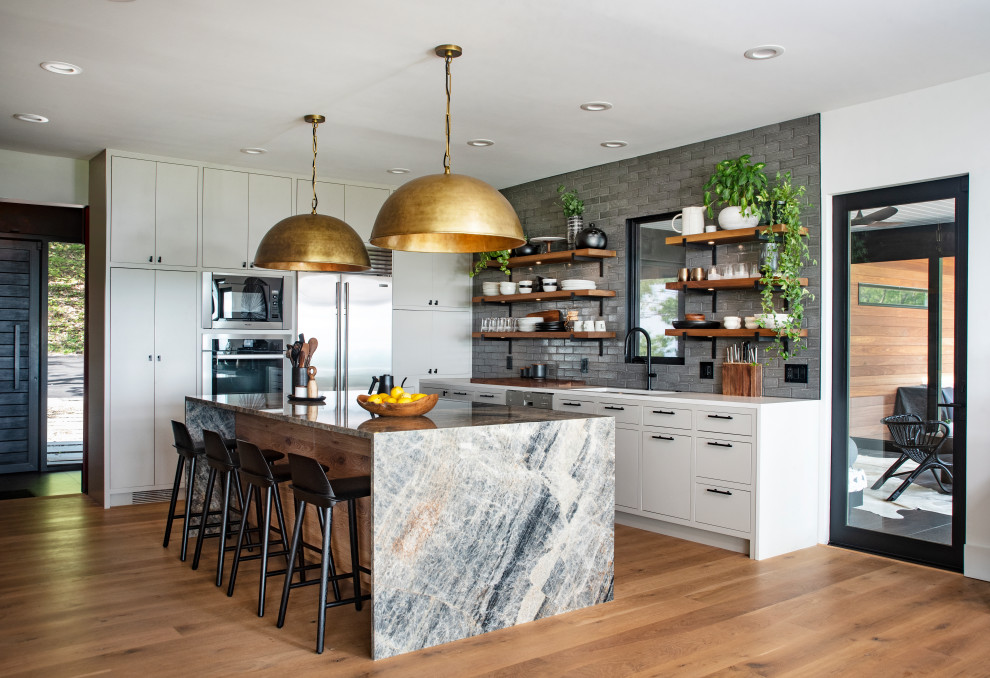 This is an example of a large contemporary kitchen in New York with flat-panel cabinets, quartz benchtops, grey splashback, ceramic splashback, stainless steel appliances, with island, an undermount sink, white cabinets, light hardwood floors and white benchtop.