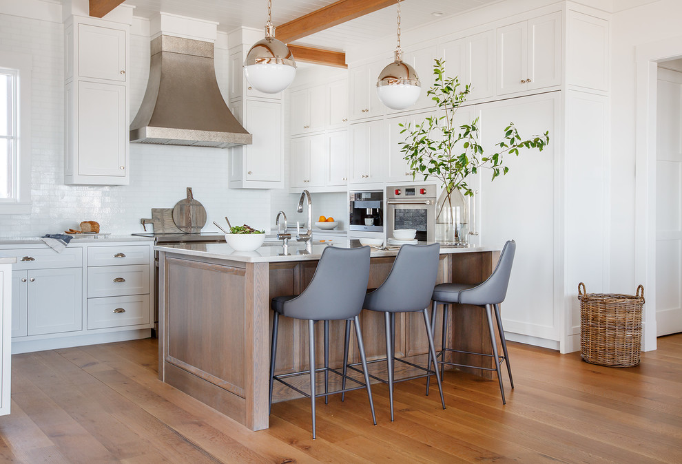 Mid-sized beach style u-shaped open plan kitchen in Jacksonville with white cabinets, white splashback, medium hardwood floors, with island, brown floor, an undermount sink, shaker cabinets, quartzite benchtops, glass tile splashback and panelled appliances.
