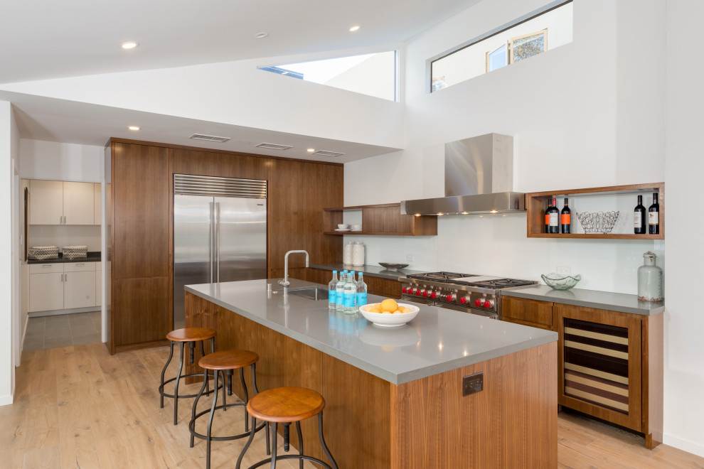 Design ideas for a midcentury kitchen in Los Angeles with a single-bowl sink, flat-panel cabinets, medium wood cabinets, stainless steel appliances, light hardwood floors, with island, grey benchtop and vaulted.
