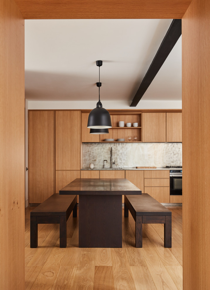 Modern inredning av ett litet linjärt kök med öppen planlösning, med en enkel diskho, luckor med profilerade fronter, skåp i mellenmörkt trä, bänkskiva i rostfritt stål, stänkskydd med metallisk yta, svarta vitvaror och mellanmörkt trägolv