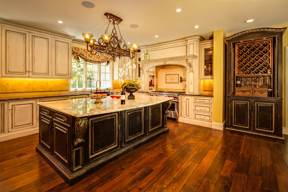 This is an example of an expansive traditional u-shaped open plan kitchen in Seattle with a farmhouse sink, white cabinets, granite benchtops, beige splashback, stone tile splashback, stainless steel appliances, medium hardwood floors and with island.