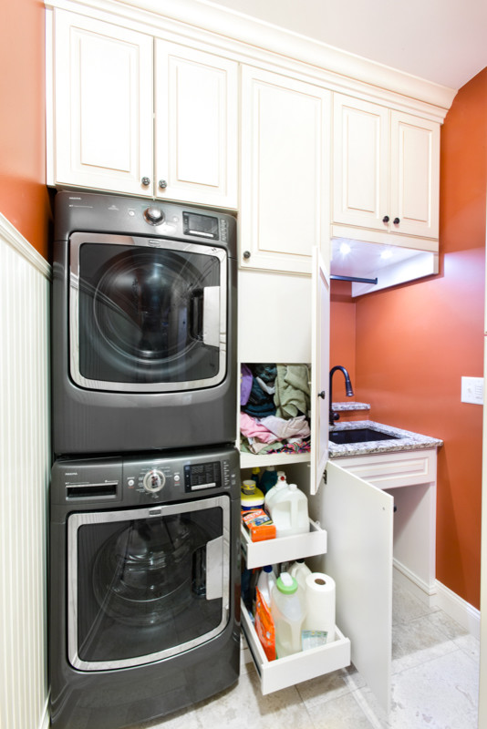 This is an example of a mid-sized traditional utility room in Chicago with an undermount sink, raised-panel cabinets, white cabinets, granite benchtops, orange walls, ceramic floors and a stacked washer and dryer.