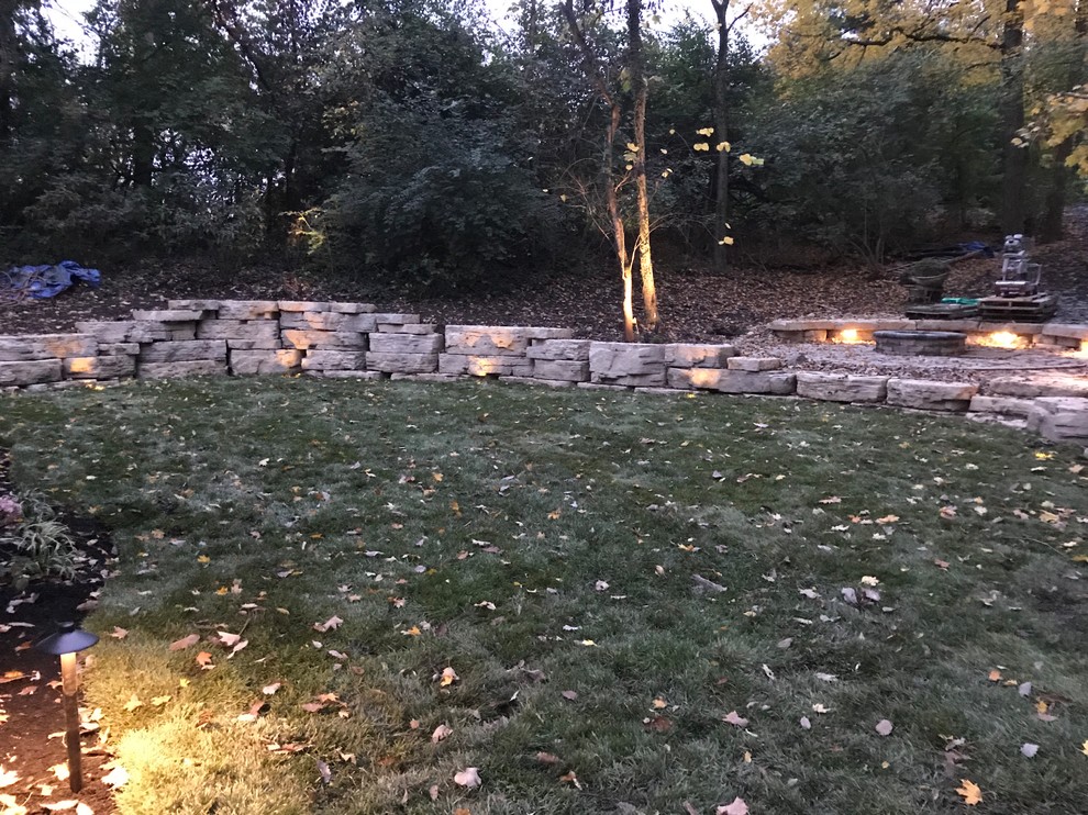 This is an example of a large rustic shade backyard concrete paver retaining wall landscape for summer.