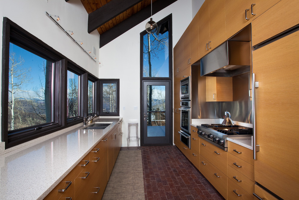 Mid-sized contemporary galley separate kitchen in Denver with an undermount sink, flat-panel cabinets, medium wood cabinets, metallic splashback, panelled appliances and brick floors.